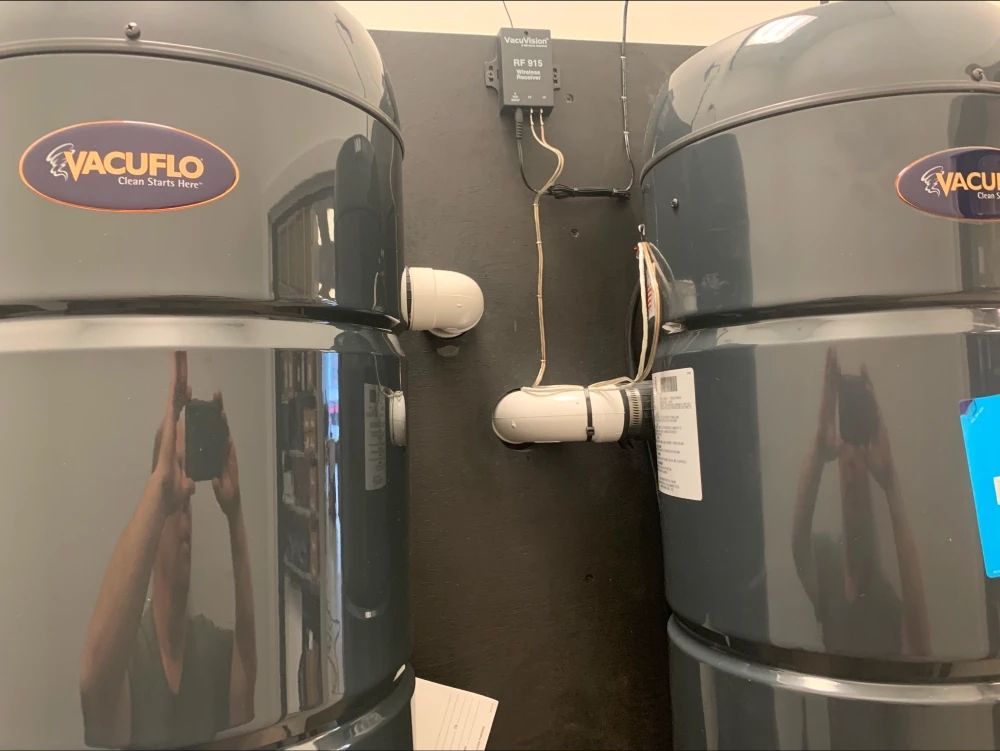 Two Vacuflo central vacuum units mounted on a dark wall with hose inlets and an electrical box.