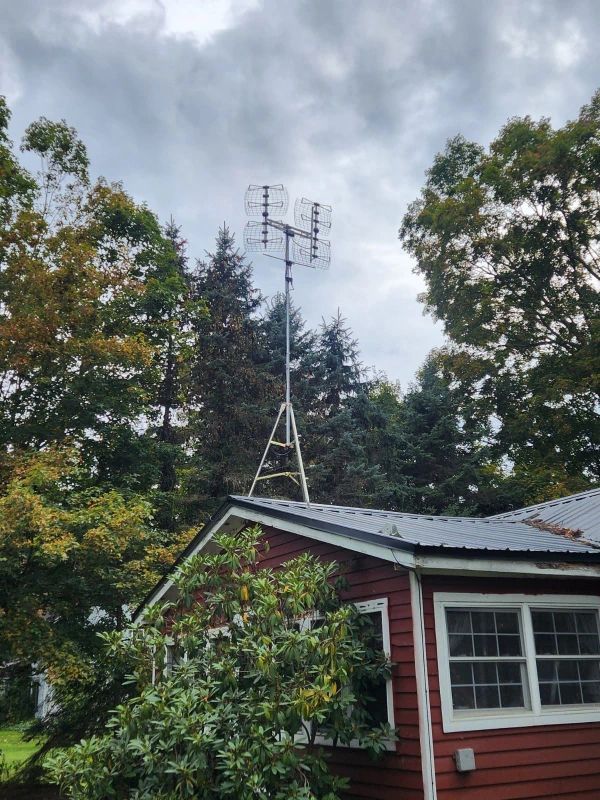 Antenna array on a tower above a red house, surrounded by trees under a cloudy sky.