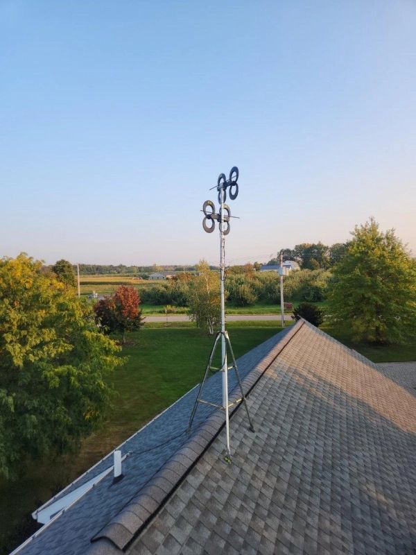 White antenna on a roof, composed of eight circular elements; rural landscape in background.