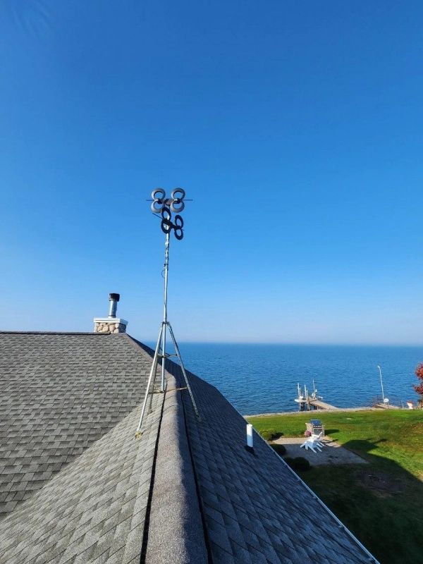 A tall tripod with a device on top sits on a roof overlooking a blue lake.