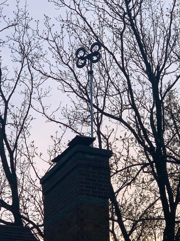 Chimney with decorative metal circles on a pole, silhouetted against a cloudy sky and tree branches.