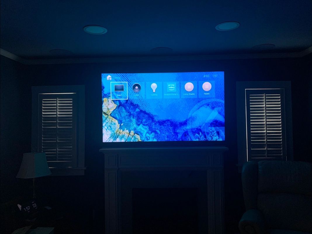 Large TV on a fireplace mantel, flanked by windows with shutters. Blue-lit room.