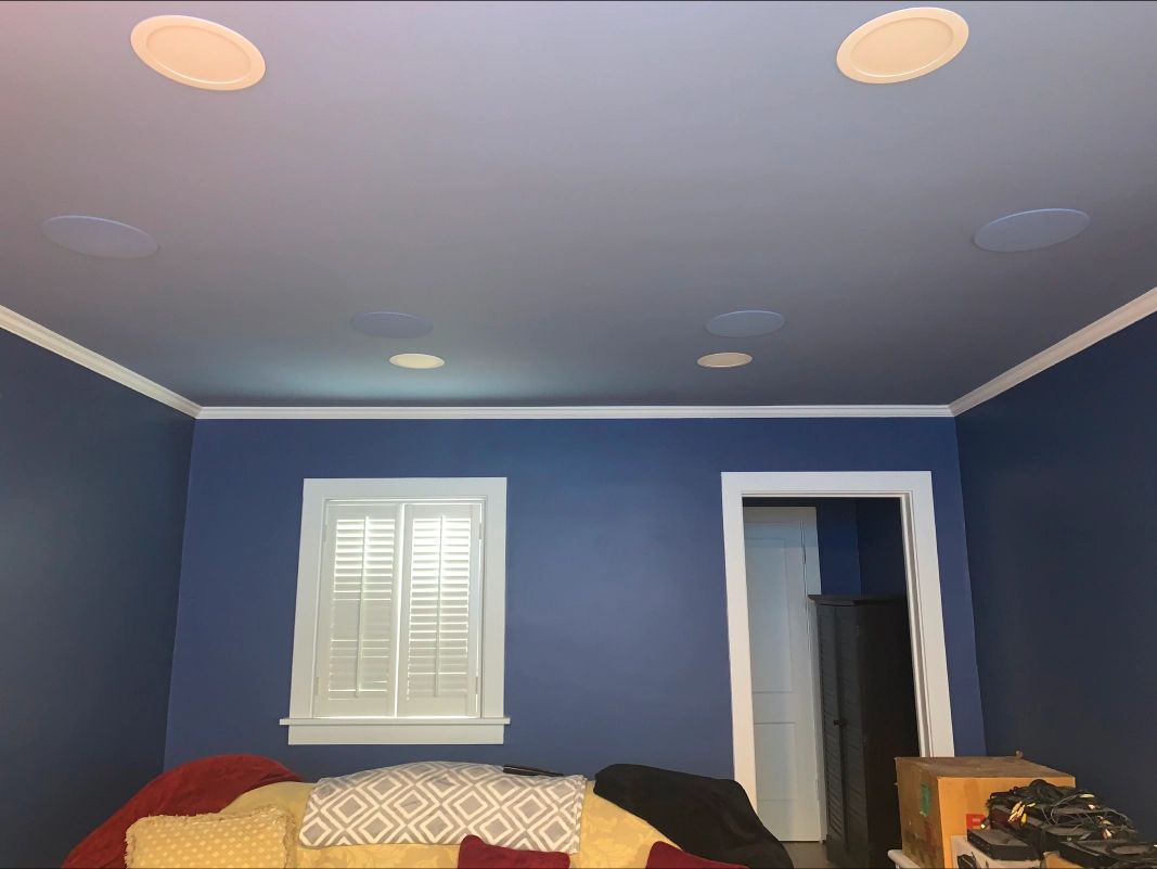 Blue room with white trim, ceiling speakers, window, and doorway. A yellow couch is in front of the window.