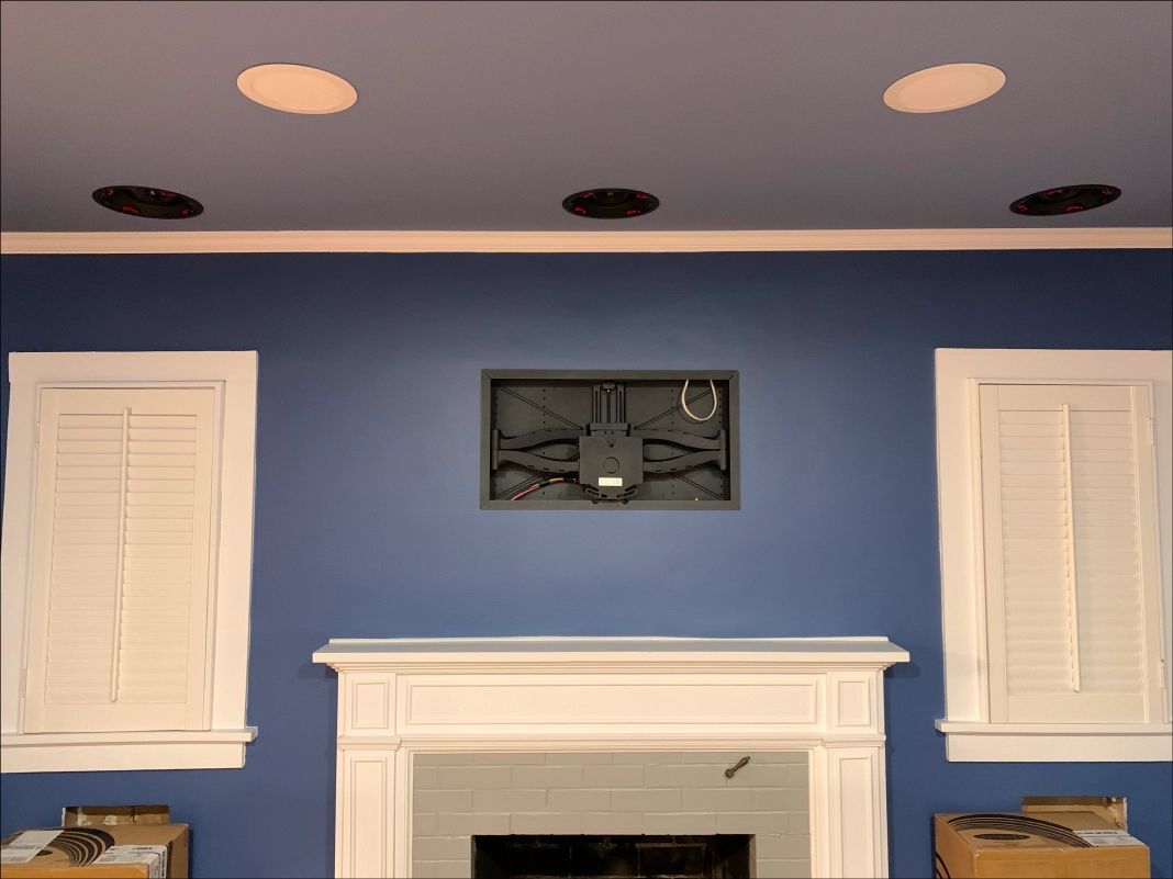 Blue wall with white fireplace and shutters; TV mount above; recessed ceiling lights.
