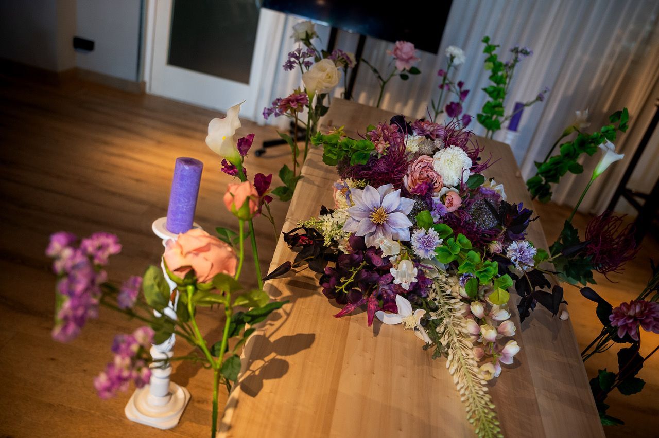 Kistbedekking van zijden bloemen in paars, wit en oudroze op een lichte houten kist