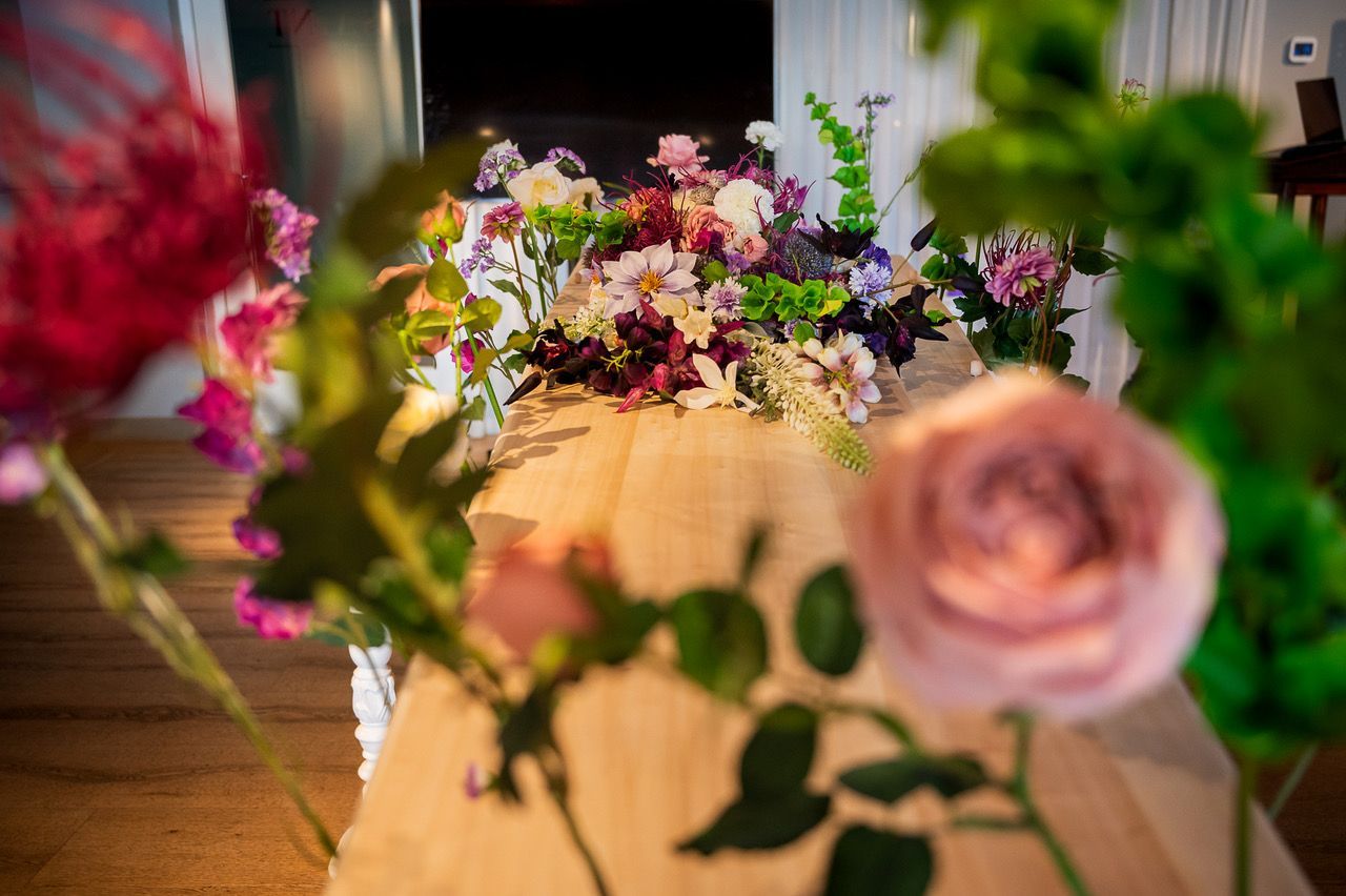 Kistbedekking van zijden bloemen op een lichte houten kist, gezien tussen de stelen van de bloemenband door