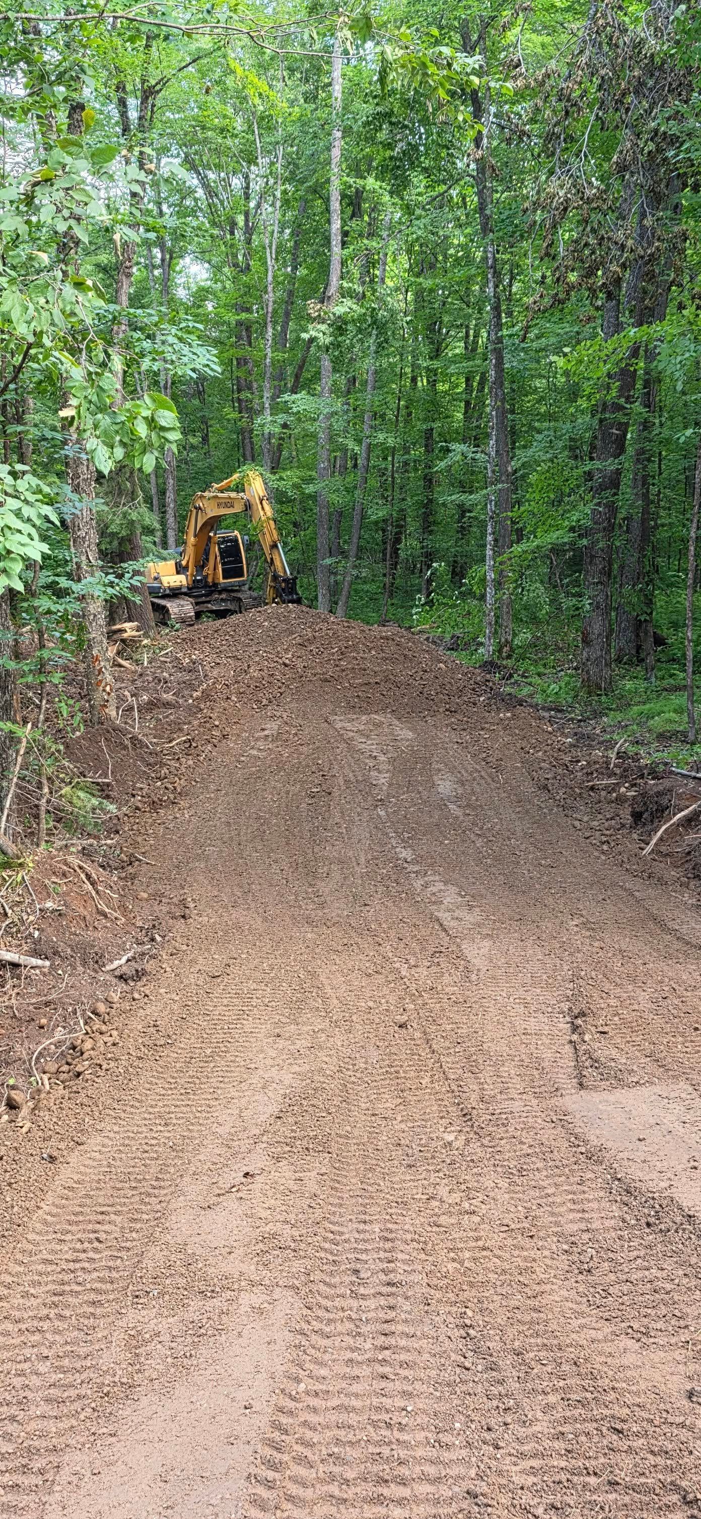 A yellow excavator parked atop a mound of dirt in a dense, green forest.