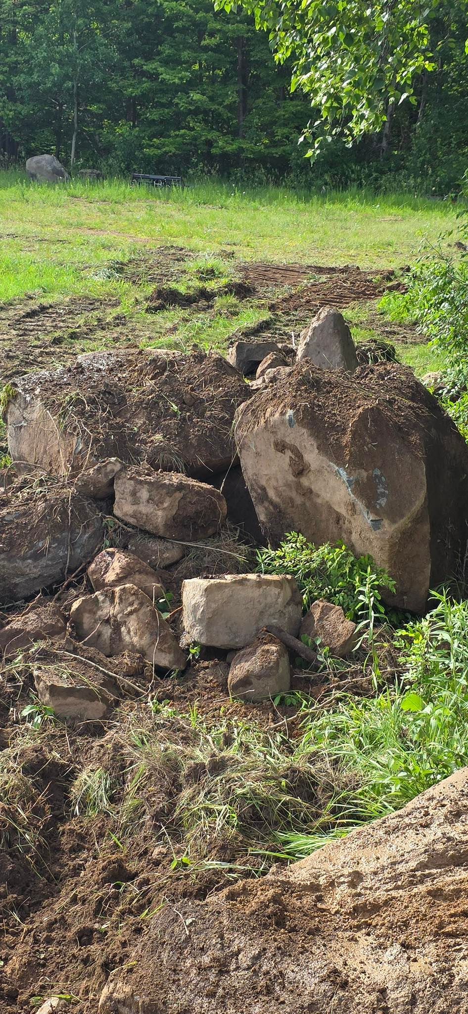 A pile of large, broken concrete chunks and rocky debris sits in a grassy, wooded outdoor area.