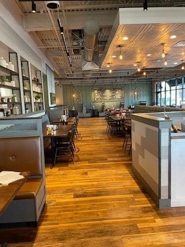 Modern restaurant interior with wooden floors, booths, tables, and pendant lights
