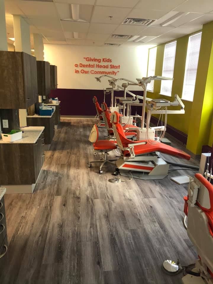 Dental clinic treatment room with red dental chairs, equipment, and gray wood flooring.