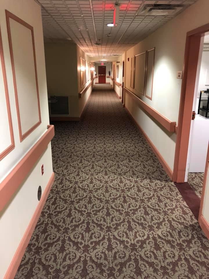 Hotel hallway with patterned carpet, beige walls, and open doors