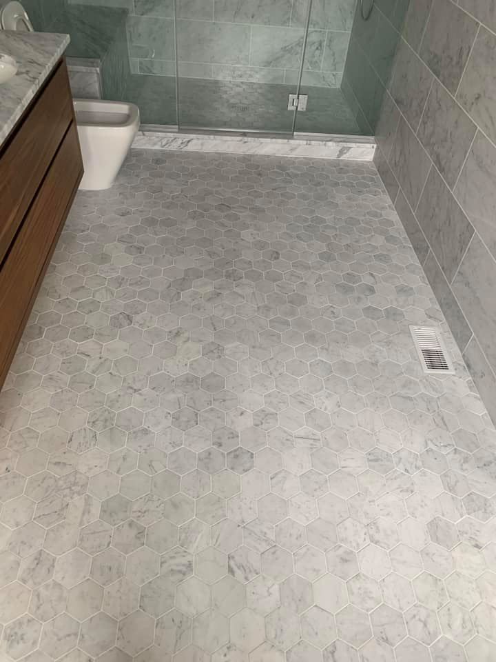 Small gray-tiled bathroom floor with a shower area and a toilet in the corner.
