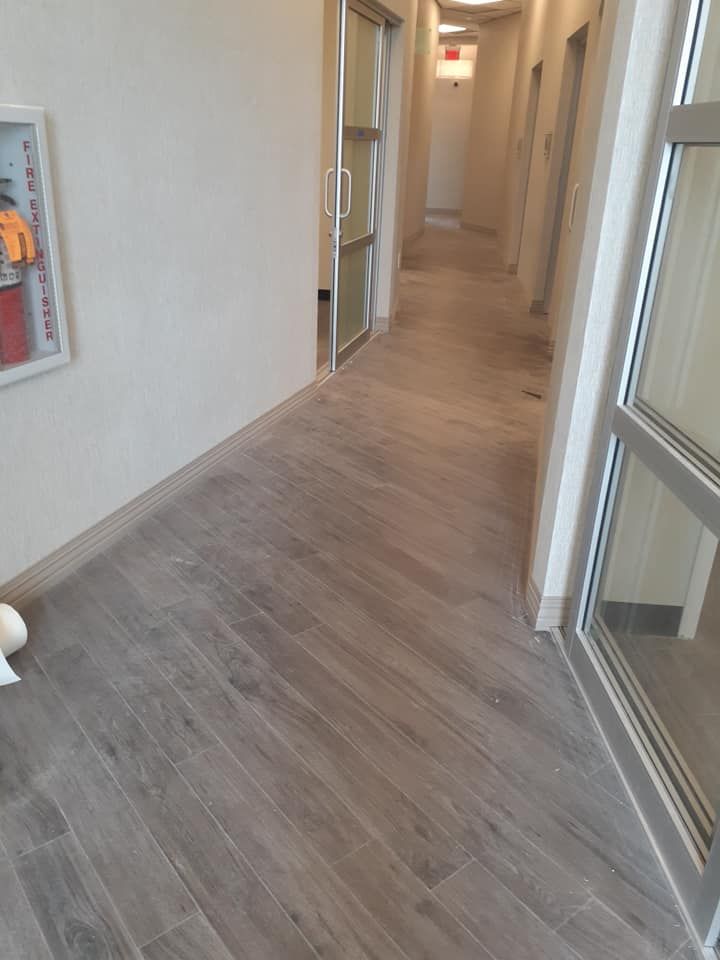 Empty beige hallway with wood-pattern flooring and glass doors on the right