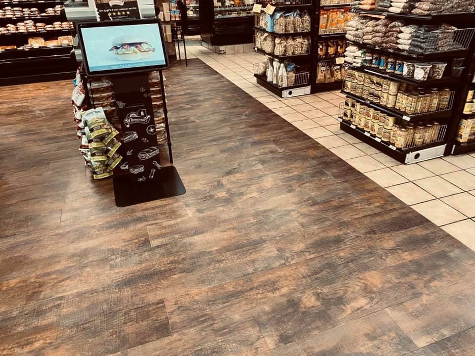 Store aisle with shelves of snacks and a small display stand on a wood-patterned floor.