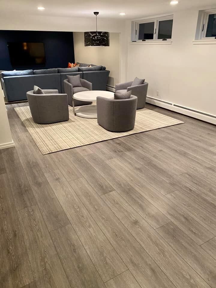 Modern living room with gray chairs, a sofa, large rug, TV, and wood flooring