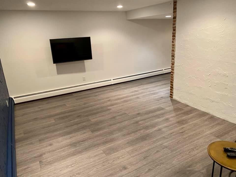 Empty modern room with gray wood flooring, wall-mounted TV, white walls, and a small round table.