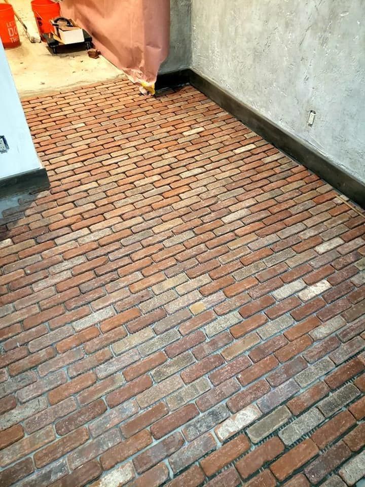 Brick-paved walkway beside a white wall, leading toward a doorway and outdoor area.