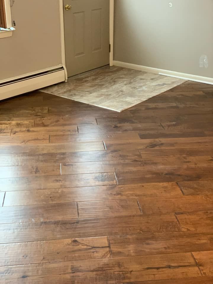 Empty room with wood flooring and a small beige tiled area near a closed door.