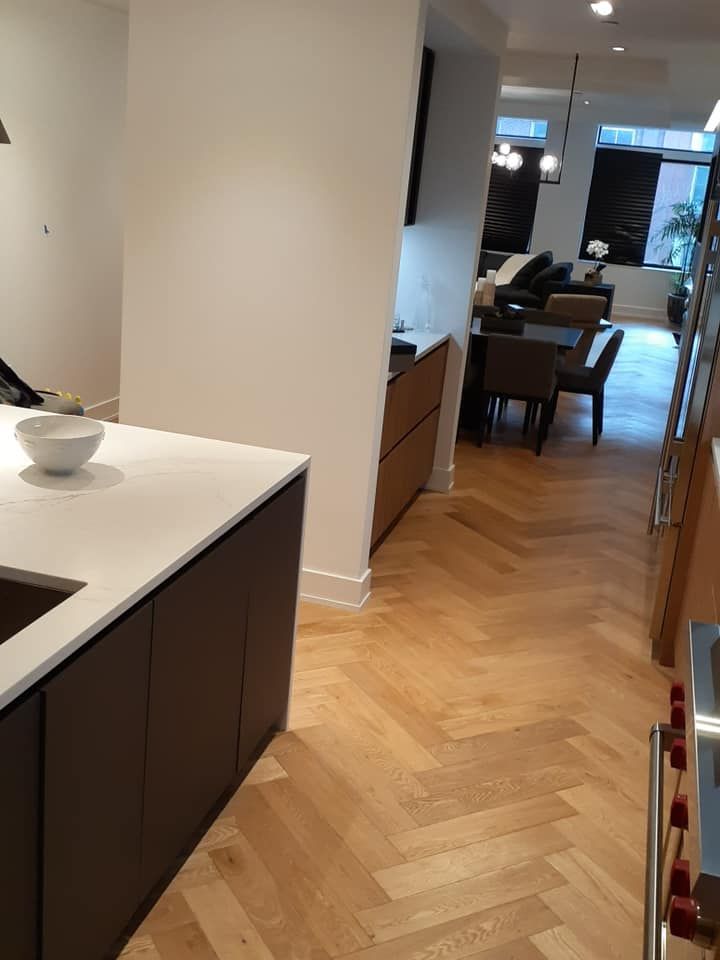 Modern kitchen with white island, herringbone wood floor, and view into a dining area with chairs.