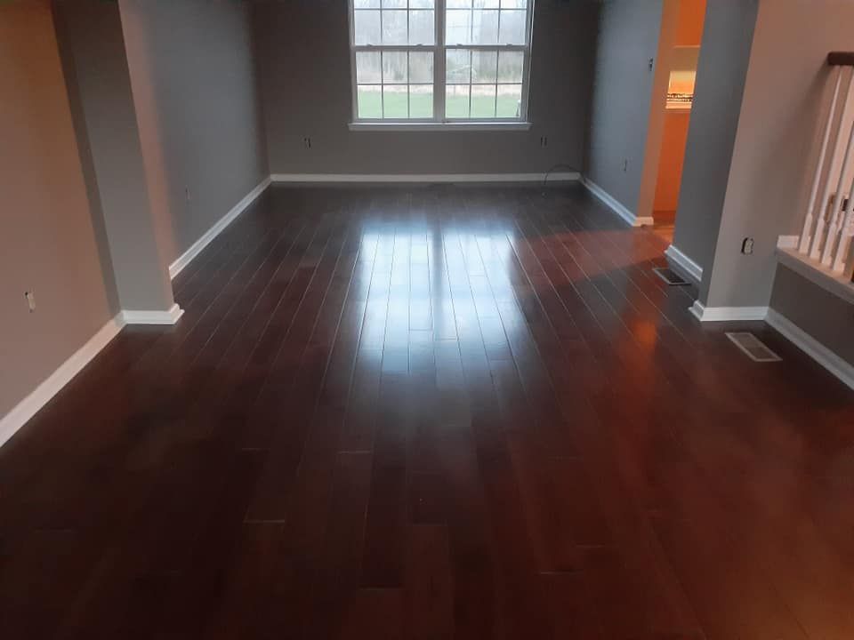 Empty room with dark hardwood floors, gray walls, and a window letting in light.