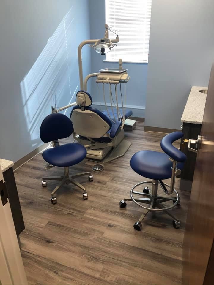Dental exam room with chair, stool, and dental equipment by a window.