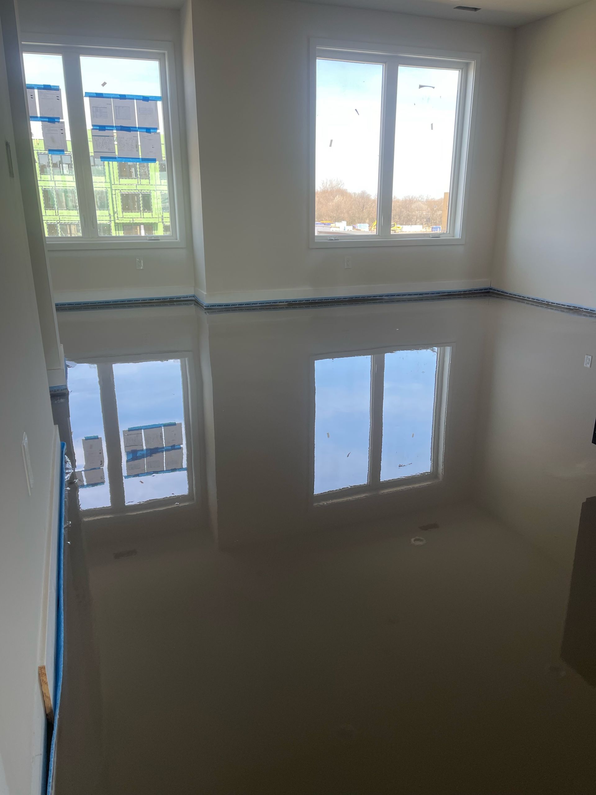 Empty room with glossy gray floor reflecting windows and daylight.