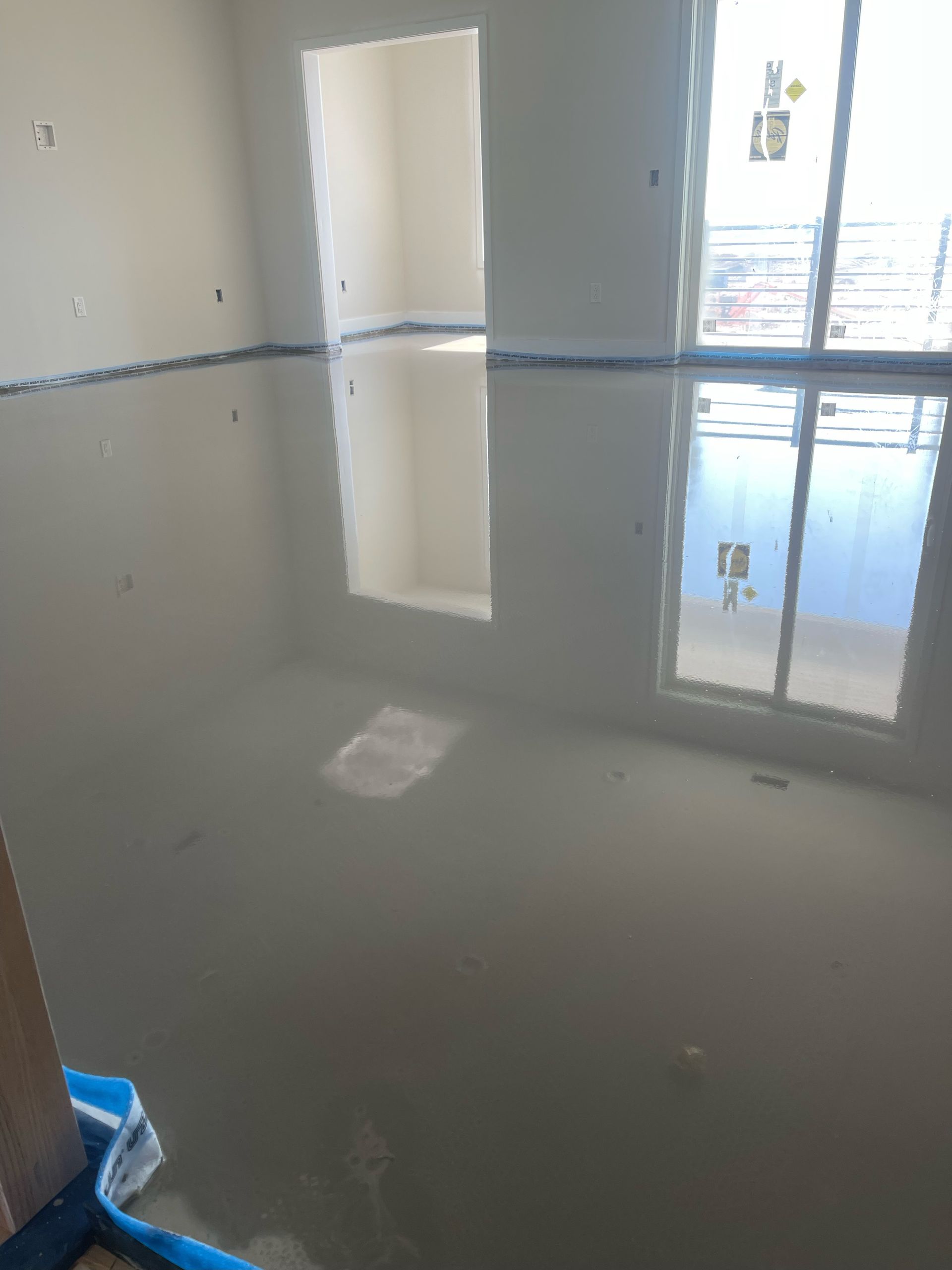 Flooded room with gray standing water reflecting a doorway and windows.