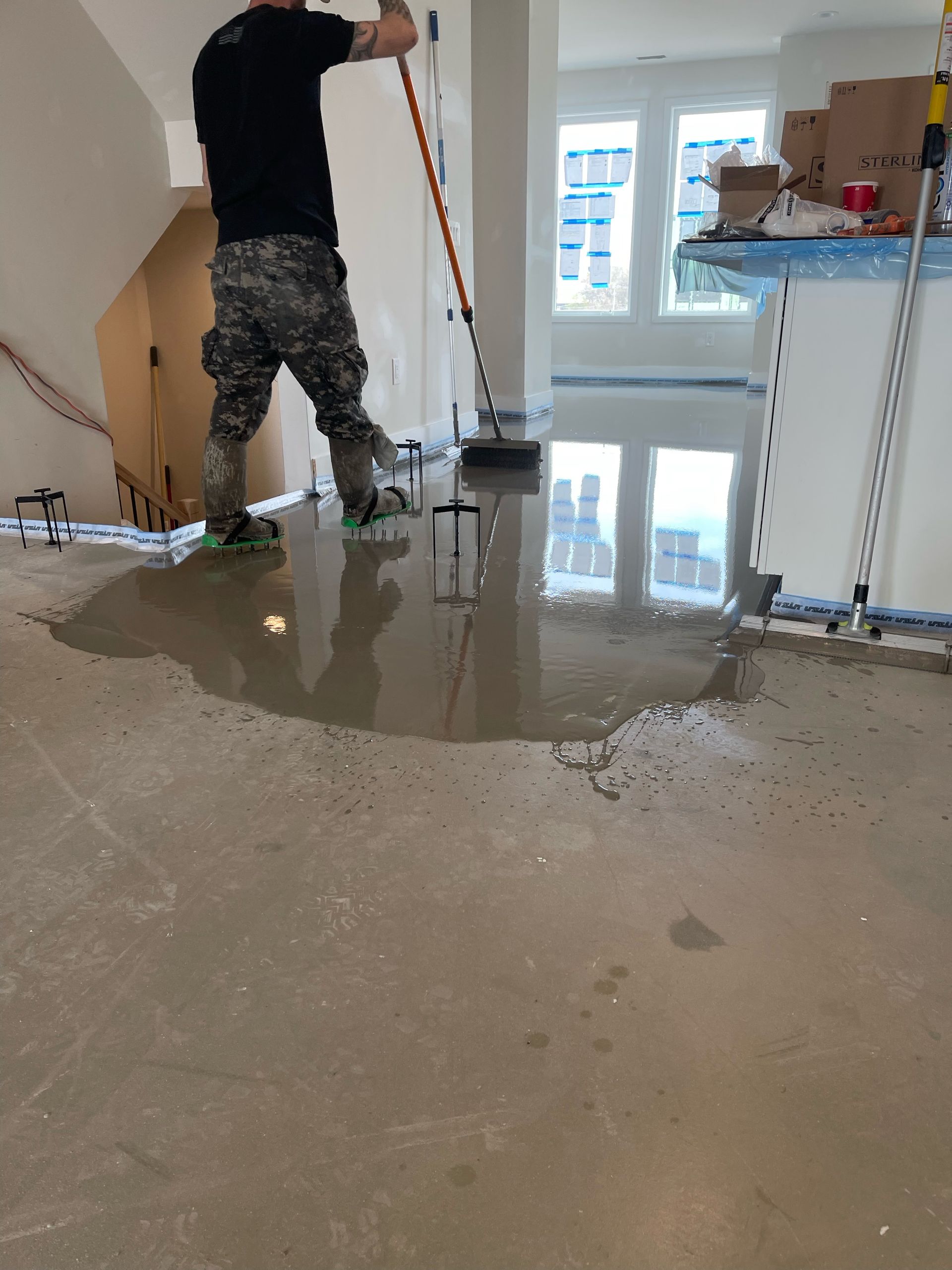 Worker leveling wet concrete floor in a bright room under renovation.