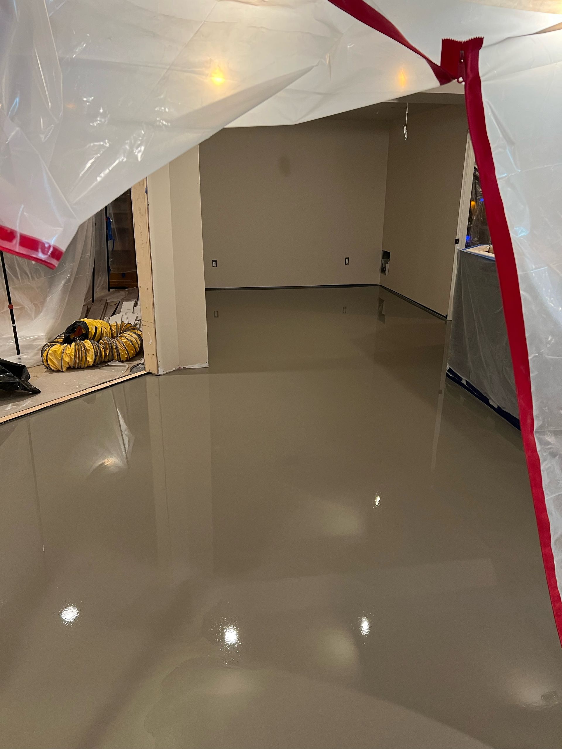 Partially finished room with glossy floor, open doorway, and plastic sheeting hanging at the entrance