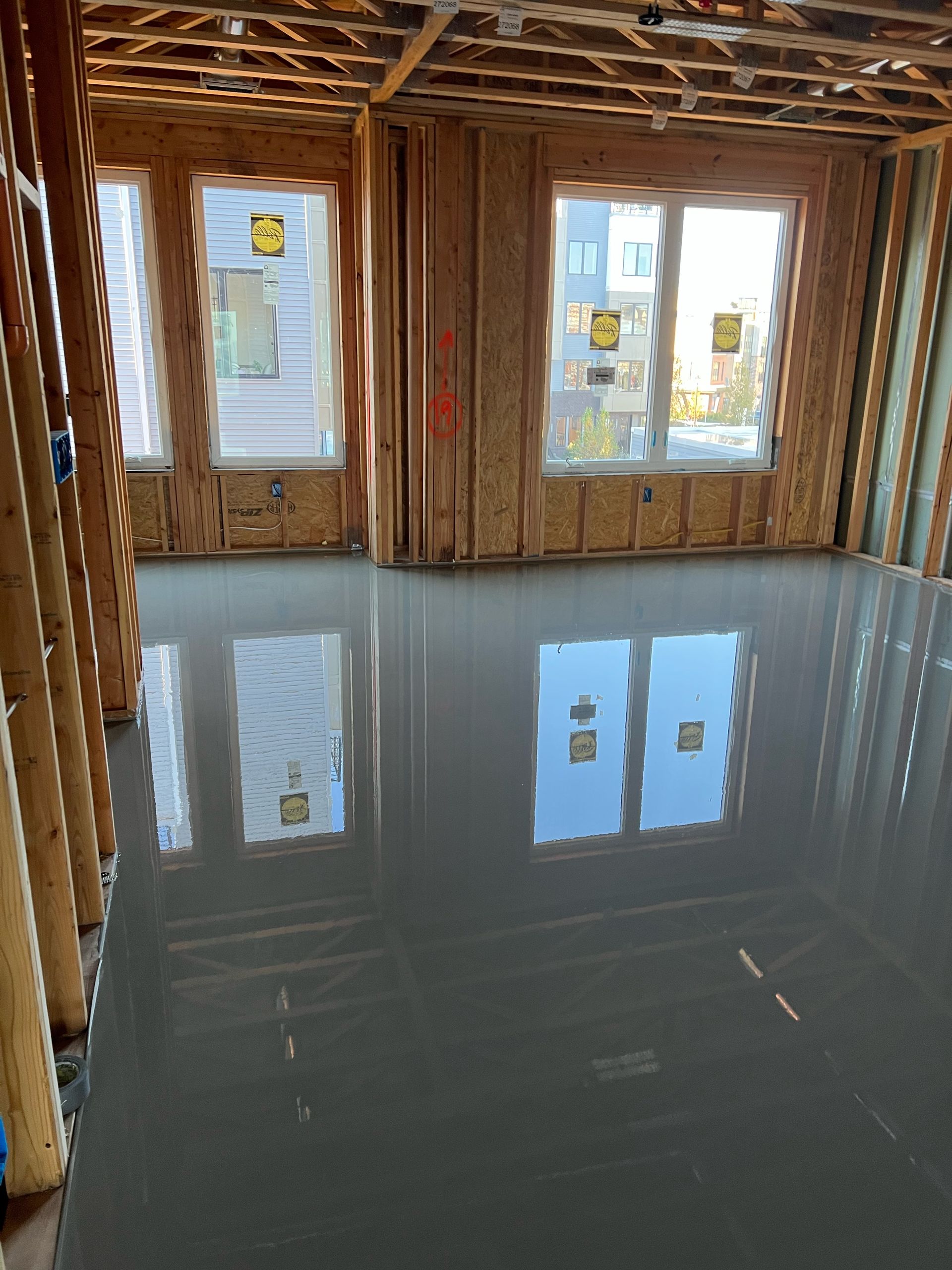 Bare unfinished room with glossy gray floor and windows reflecting daylight.