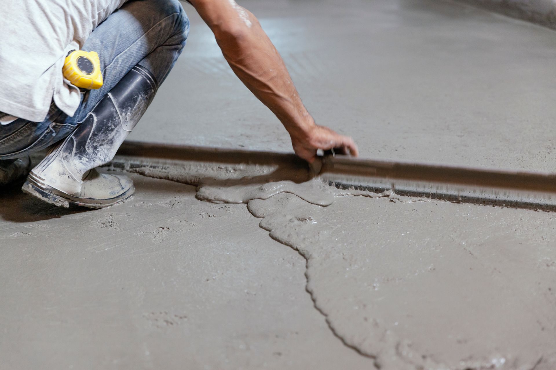 hardwood floor contractor croydon pa Worker smoothing wet concrete floor with a trowel, wearing jeans and kneepads.