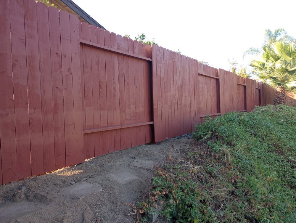 A red wooden fence is surrounded by grass and dirt.