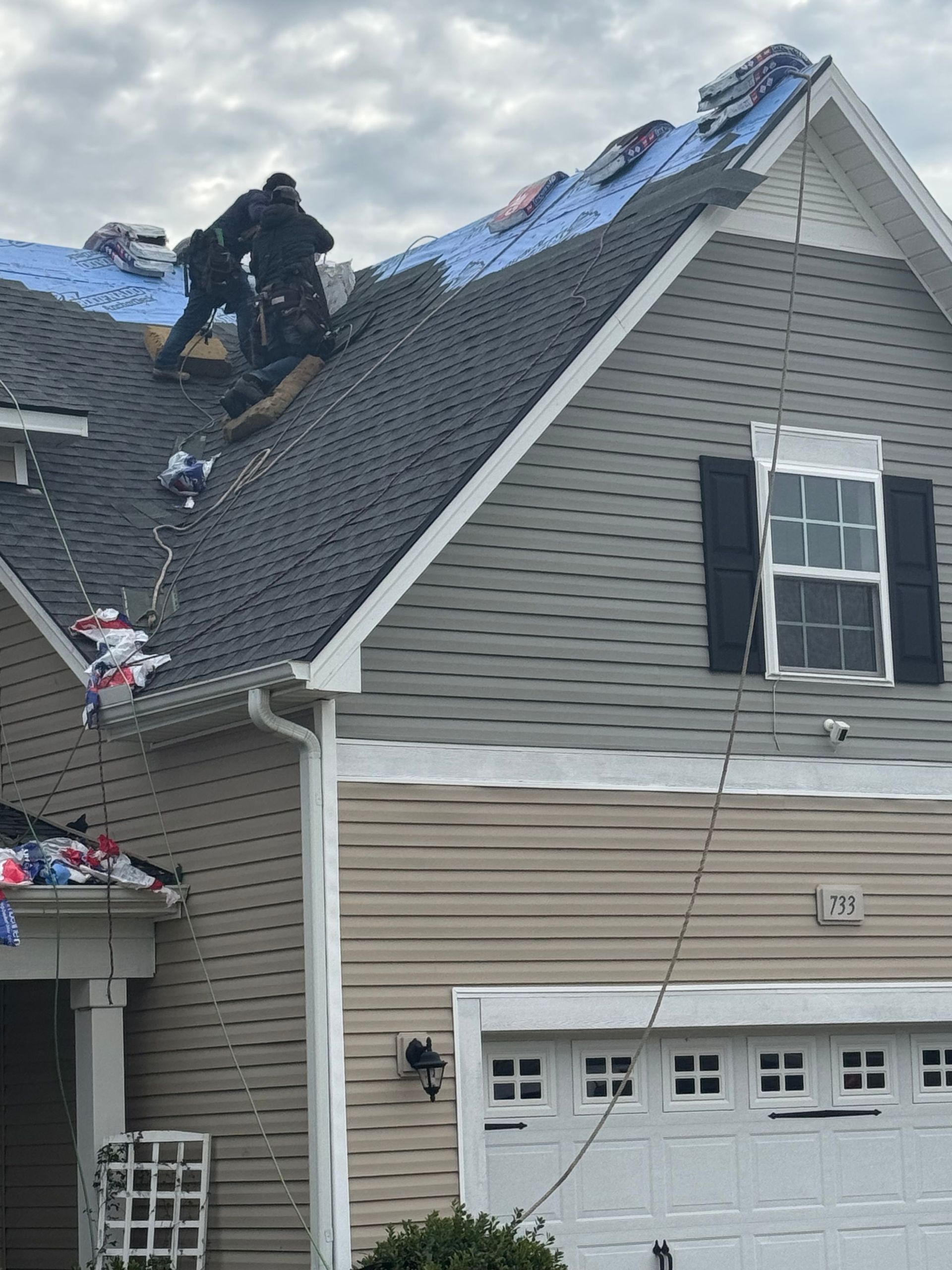 Worker repairing blue tarp-covered roof on a gray house above a garage