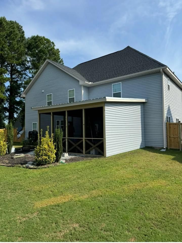 Gray two-story house with screened porch, white siding, dark roof, and green lawn under a blue sky
