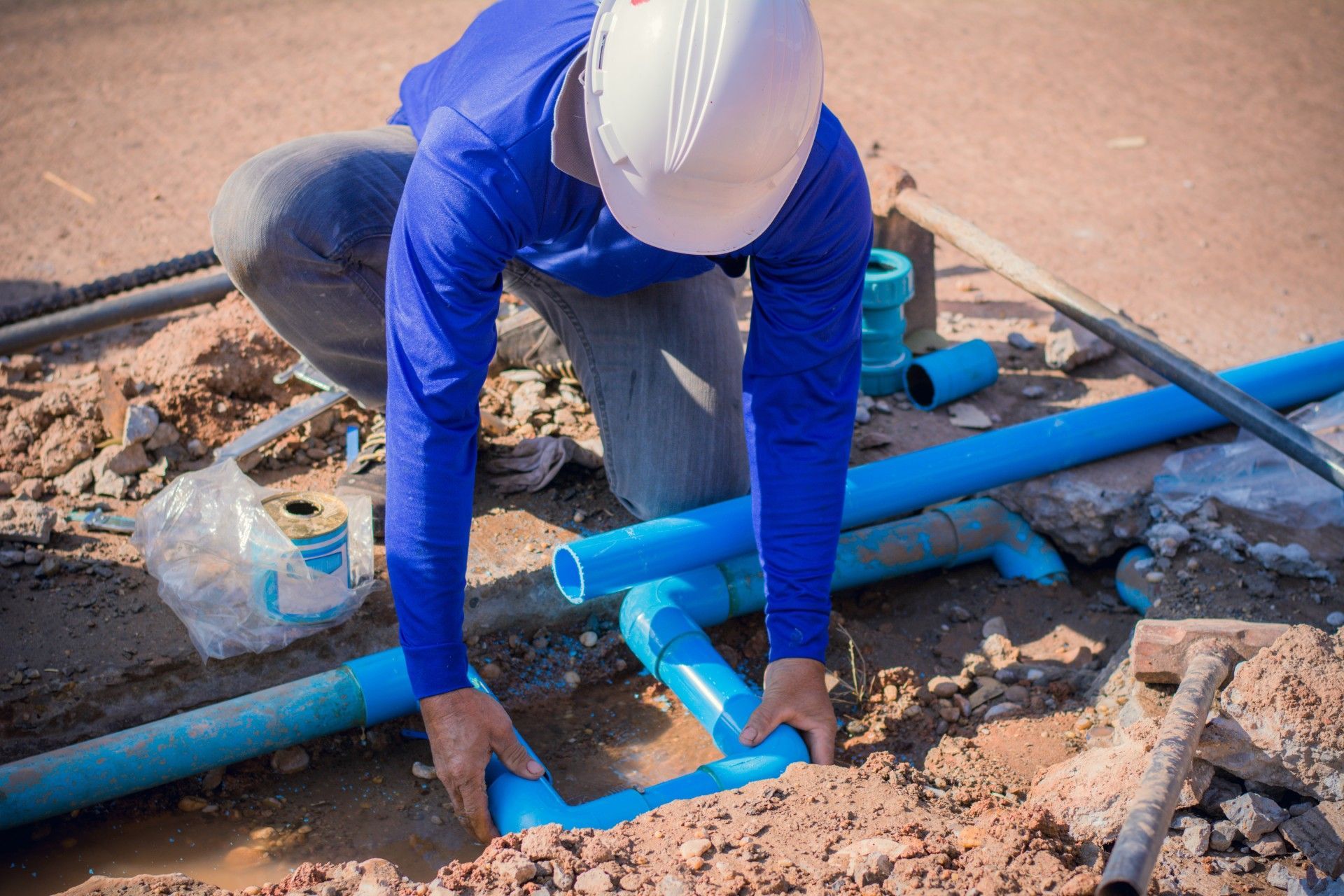 A man wearing a hard hat is working on a pipe in the dirt.
