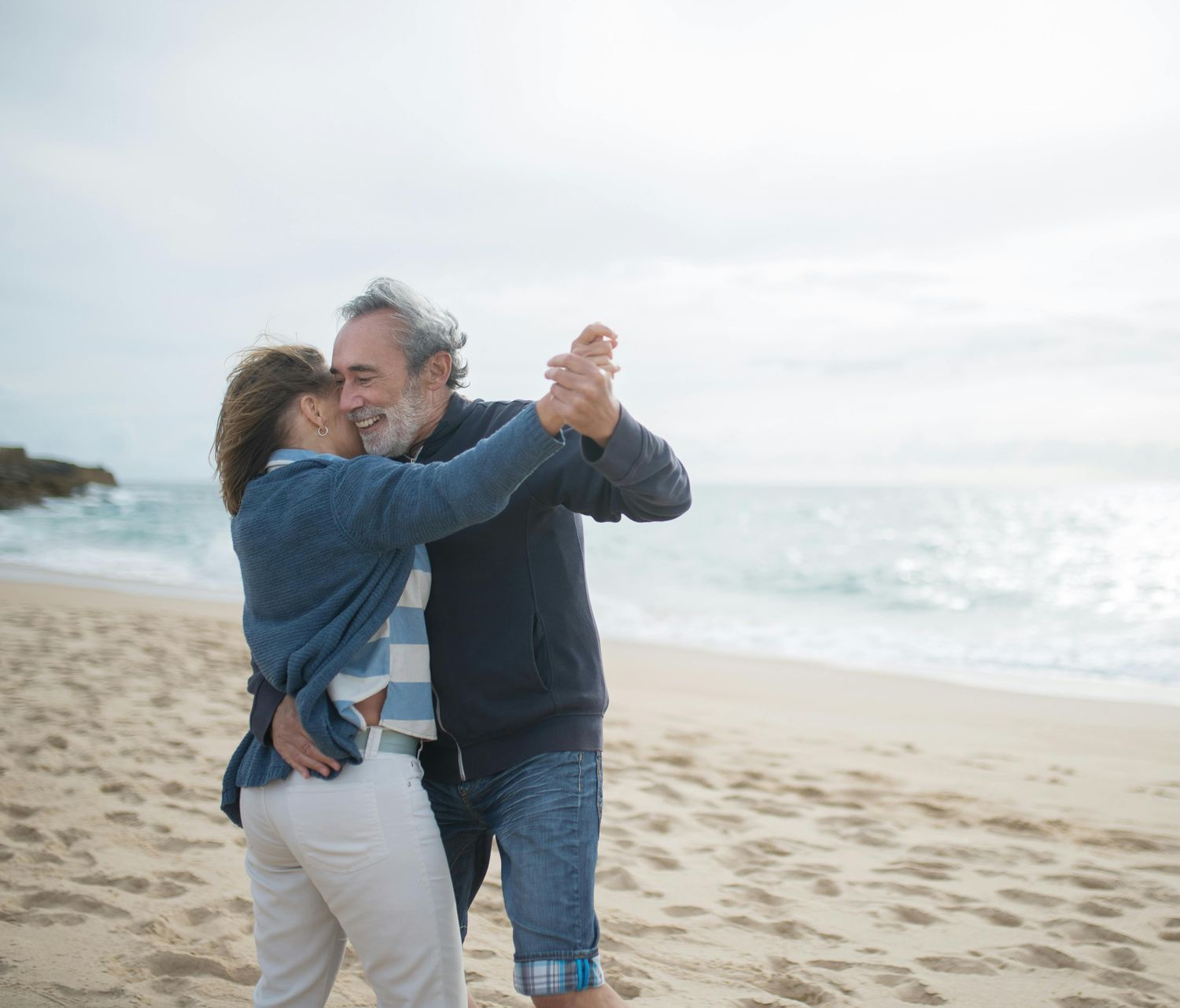 An older couple is dancing on the beach.