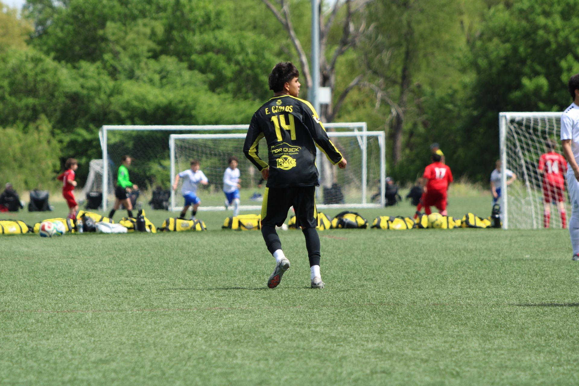 Soccer player in black and yellow jersey standing on a field near the goal, with spectators in the background