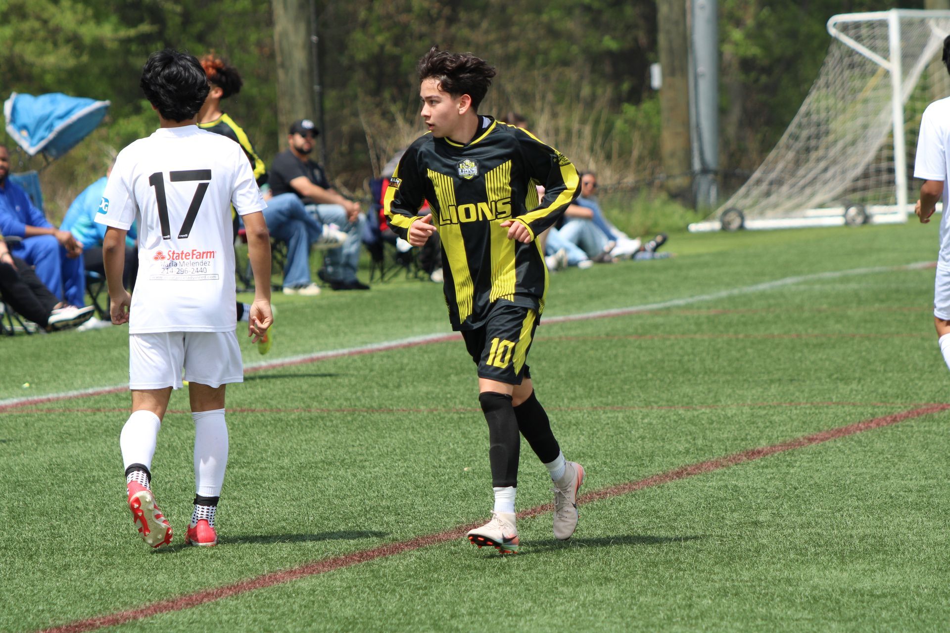 Two soccer players on a field, one in black and yellow facing a player in white near the goal.