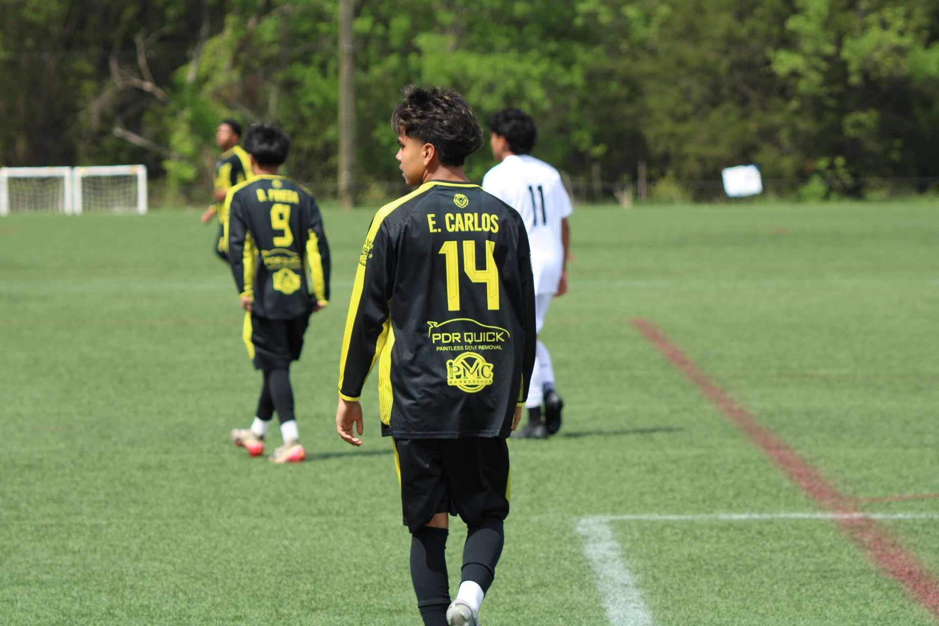 Soccer players in black and yellow jerseys walking on a grassy field during practice