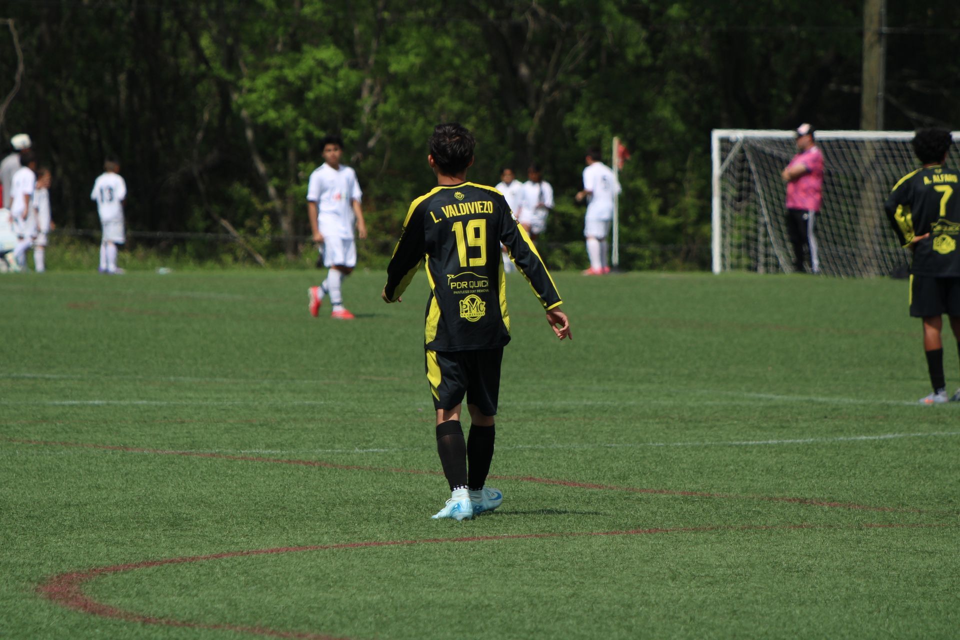 Soccer players on a wet field, with a yellow-black player facing the goal and others in white nearby