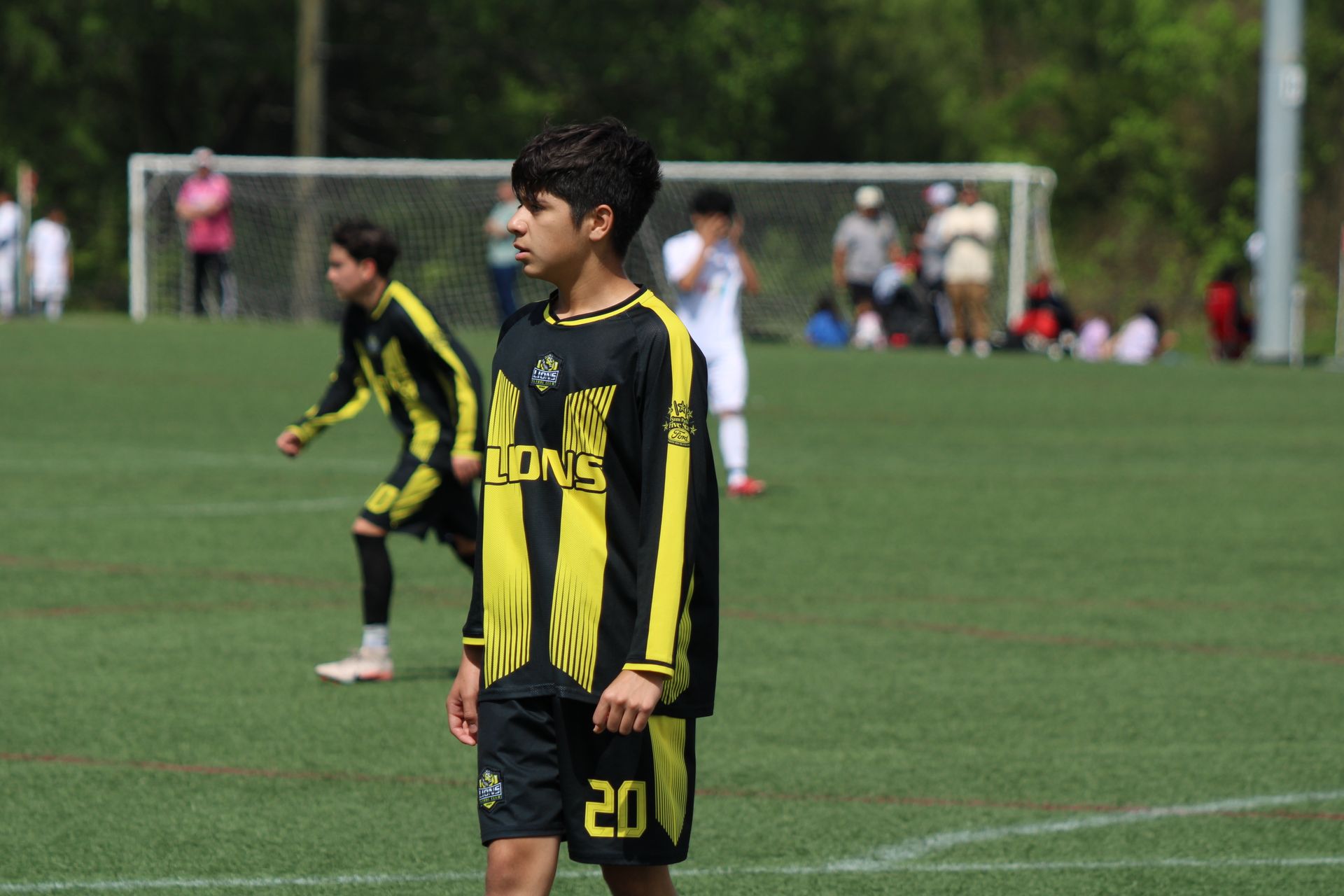 Youth soccer players in black-and-yellow uniforms stand on a grassy field near the goal.