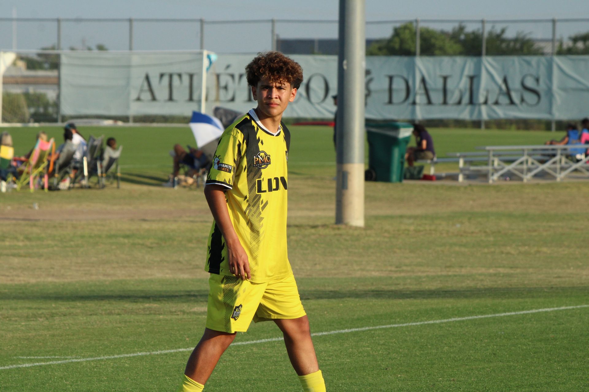 Soccer player in yellow uniform standing on a field with a stadium sign in the background