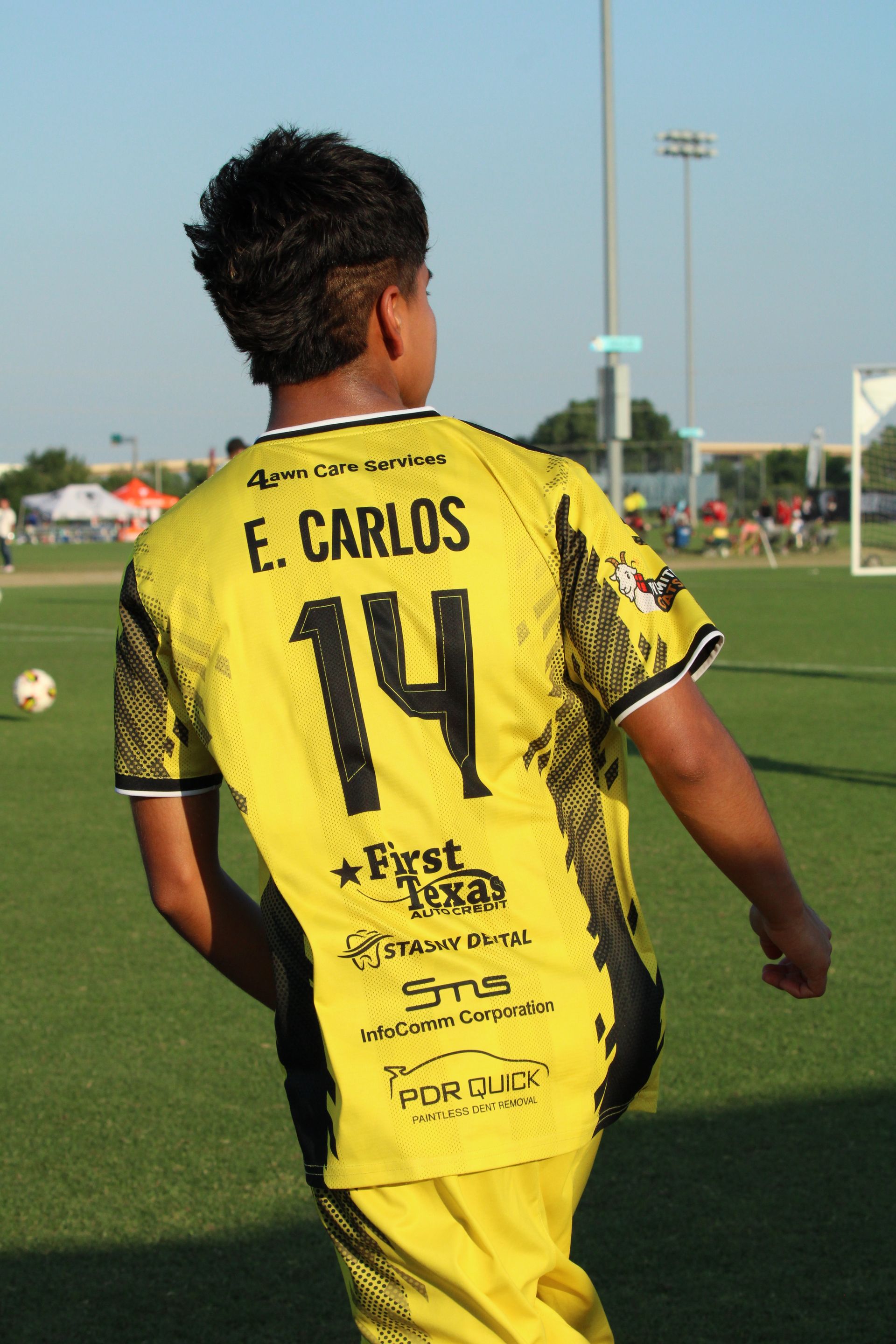 Soccer player in yellow jersey number 14 running on a field, seen from behind