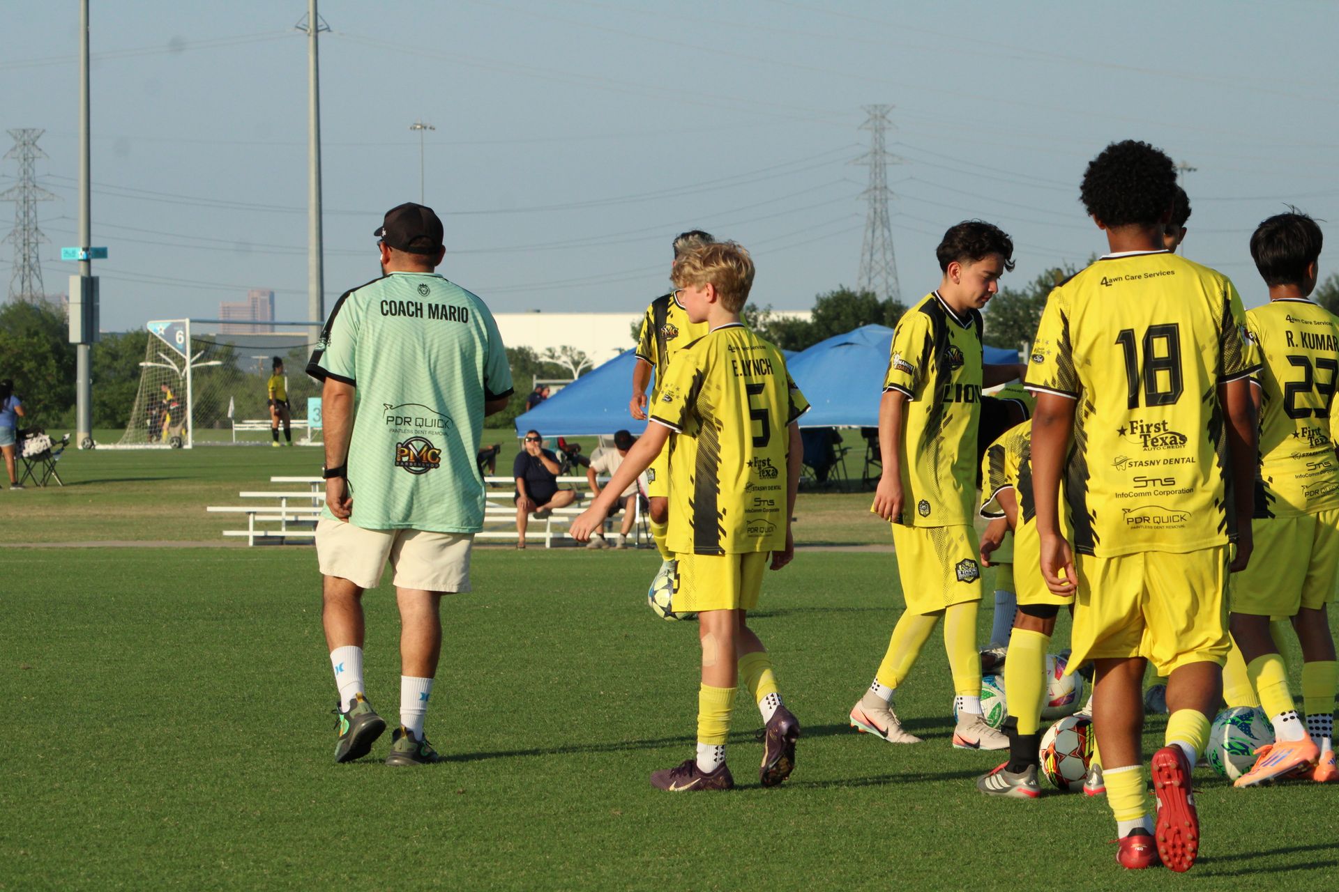 Soccer players in yellow and mint-green uniforms stand on a grassy field during a game.