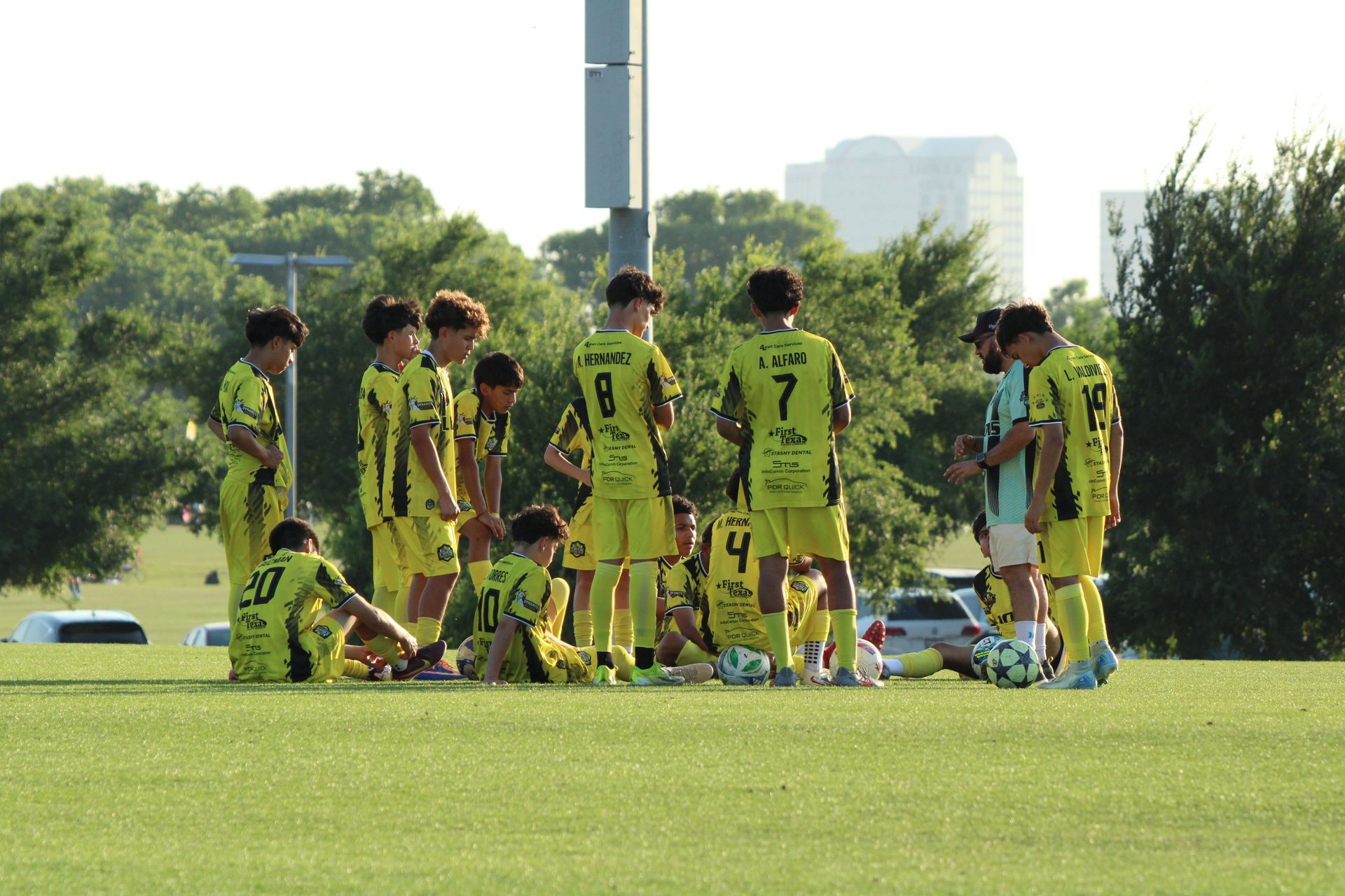 Soccer players in yellow uniforms huddle on a grassy field before practice