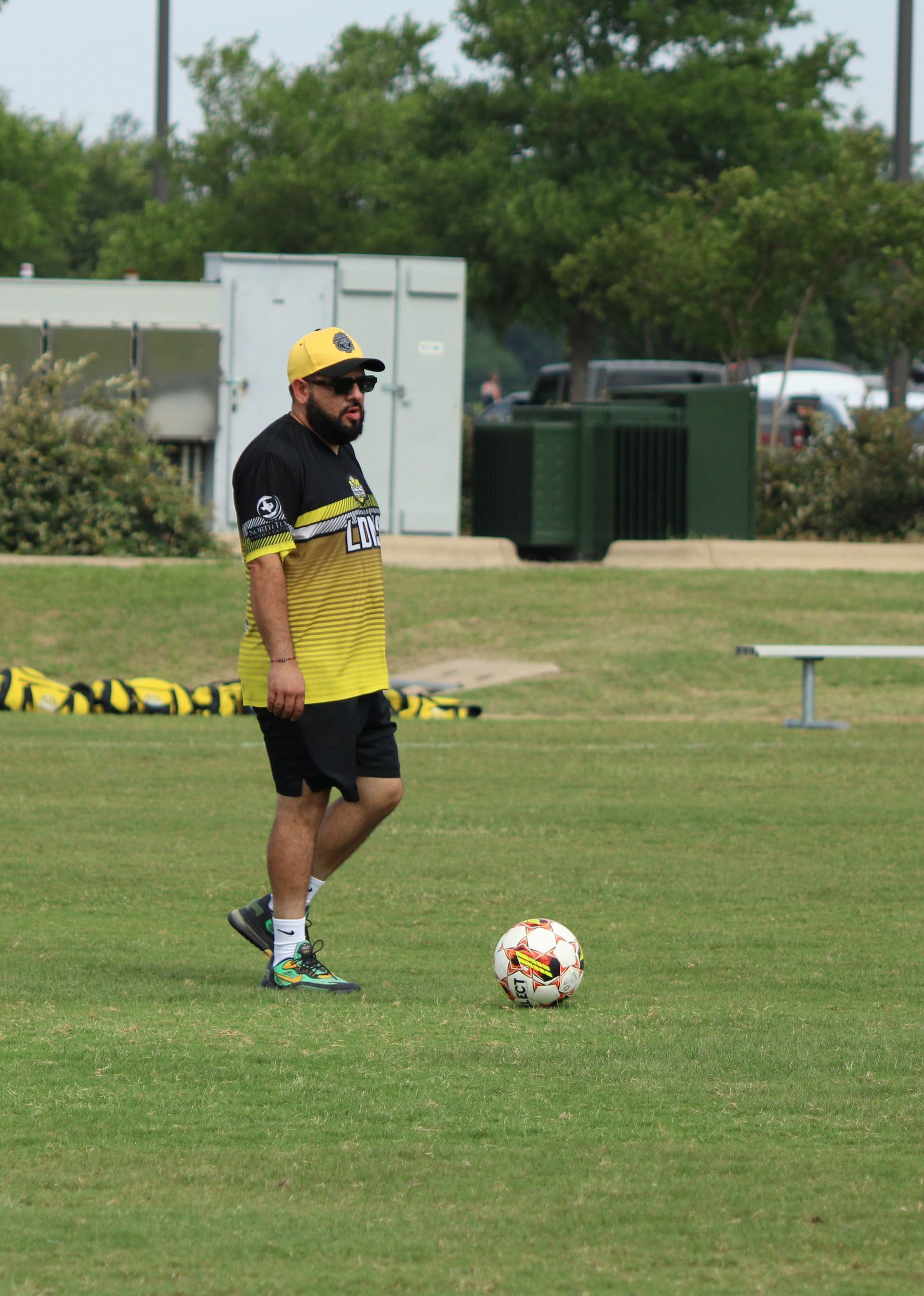 Soccer player in yellow and black stands on a grassy field near a ball and training equipment