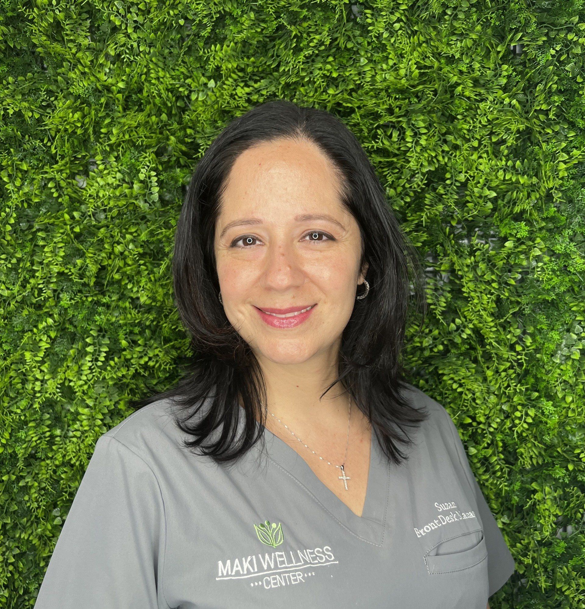 A woman in a grey scrub top is smiling in front of a green wall.