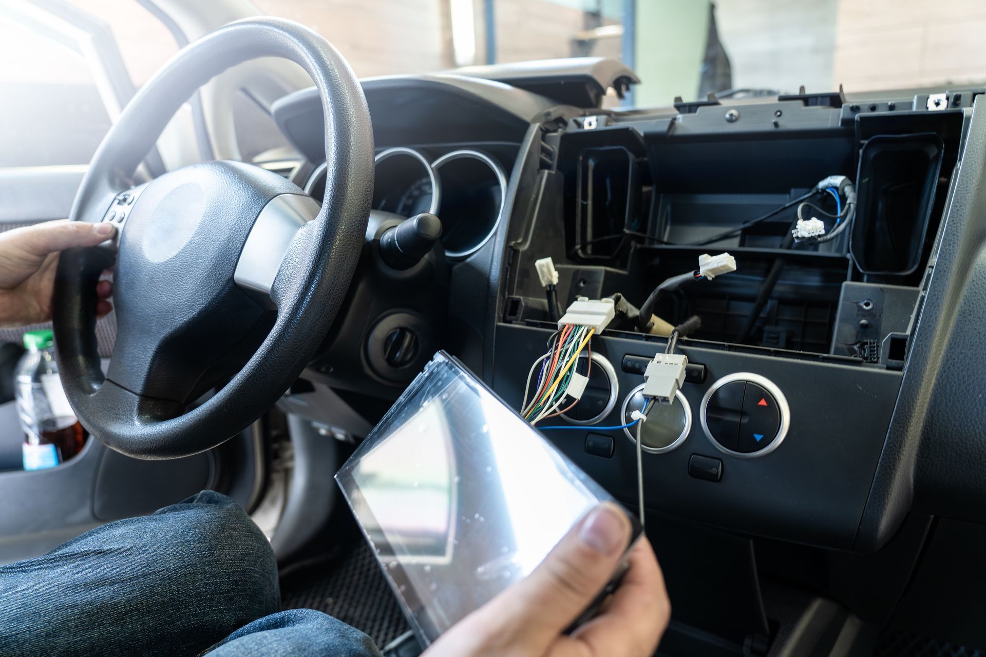 A person holds a car's replacement touchscreen head unit in front of the vehicle's opened dashboard console.