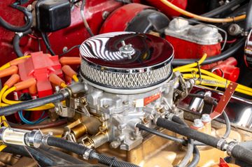A chrome-topped carburetor and air filter assembly sits atop an engine with yellow spark plug wires and red components.