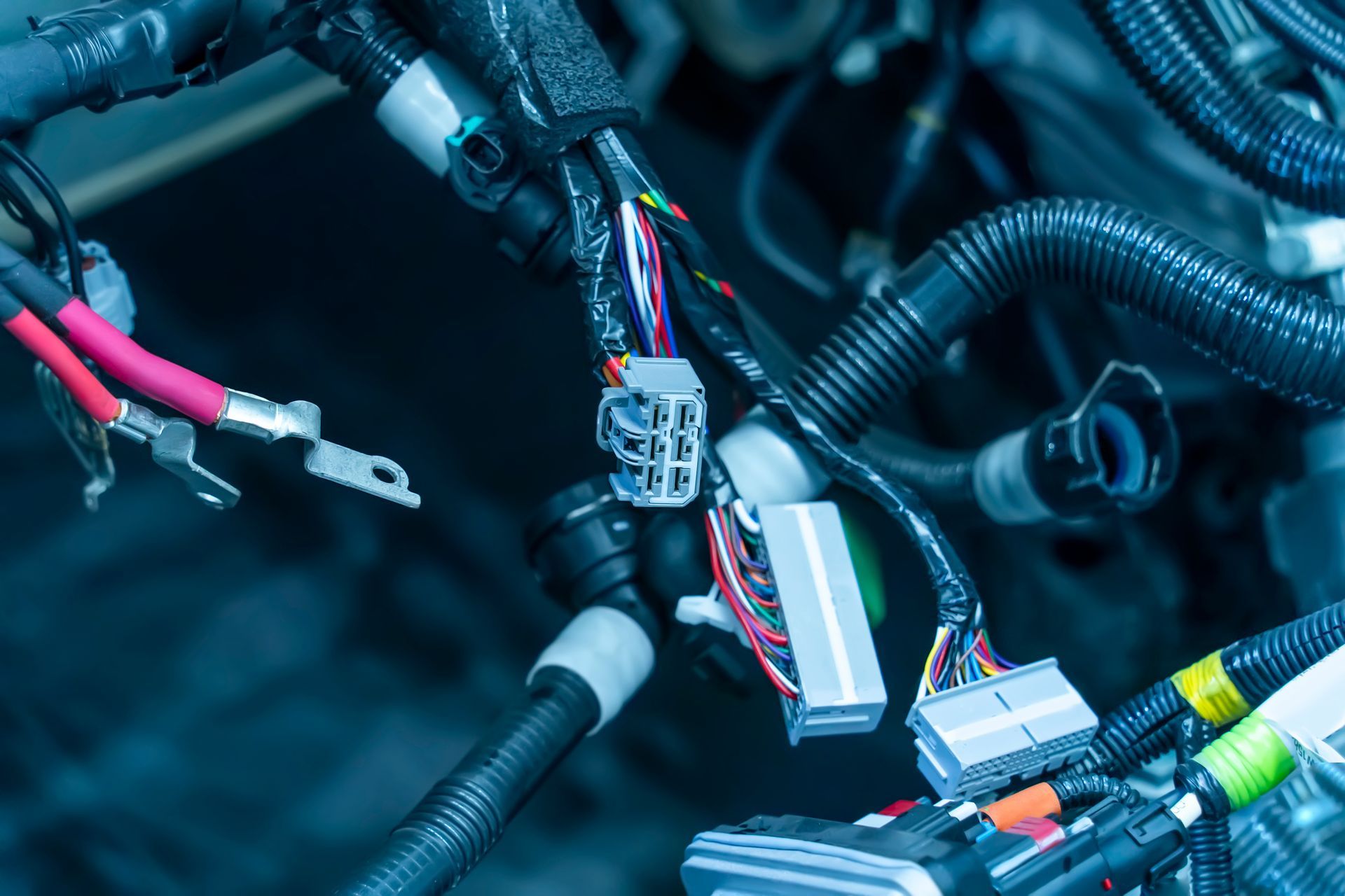 A cluster of disconnected automotive wiring harnesses and electrical connectors with multicolored wires inside an engine bay.